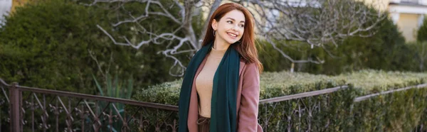Щаслива молода жінка в пальто з шарфом дивиться вбік, банер — стокове фото