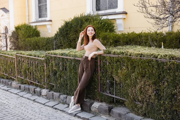 Full length of young cheerful woman listening music in wireless earphone outside — Stock Photo