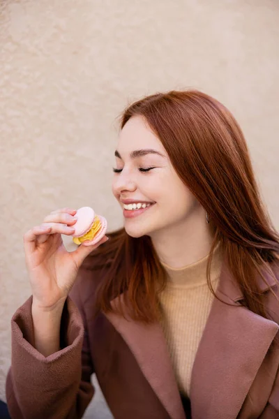 Happy young woman with red hair holding sweet macaron — Stock Photo