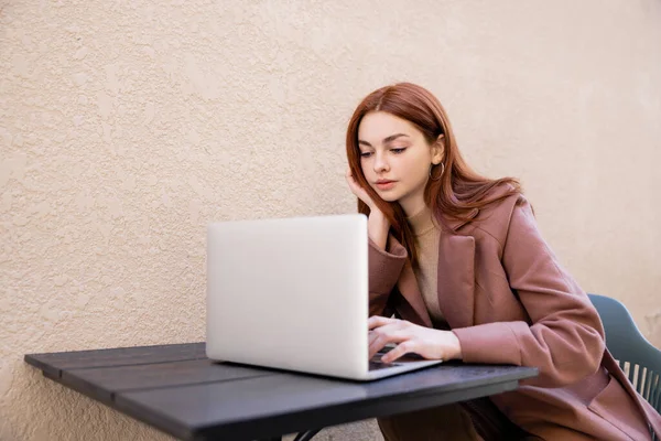 Mujer joven con el pelo rojo usando el ordenador portátil fuera - foto de stock