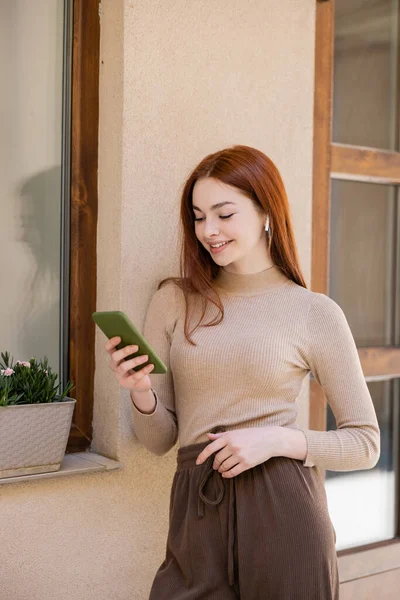 Happy redhead woman in wireless earphone holding smartphone and listening music — Photo de stock