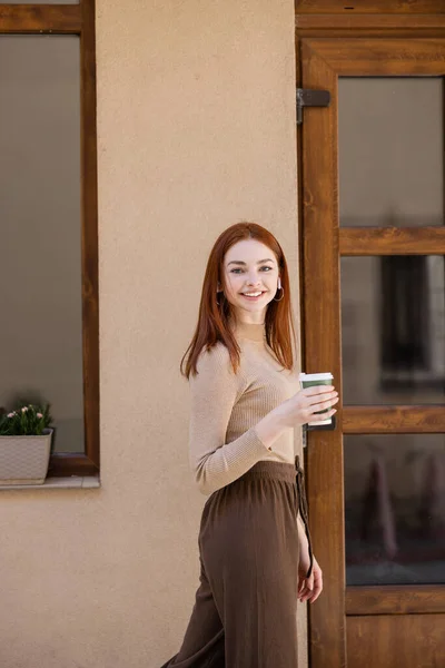 Felice giovane donna in auricolare wireless in possesso di tazza di carta — Foto stock