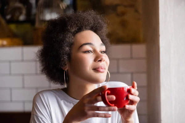 Femme afro-américaine bouclée dans des boucles d'oreilles cerceau tenant tasse de café — Photo de stock