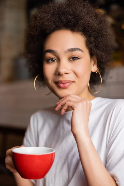 Sorrindo mulher afro-americana em brincos de argola segurando xícara de café — Fotografia de Stock