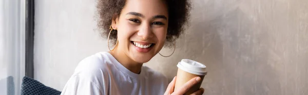 Happy african american woman in white t-shirt holding paper cup, banner — Stock Photo