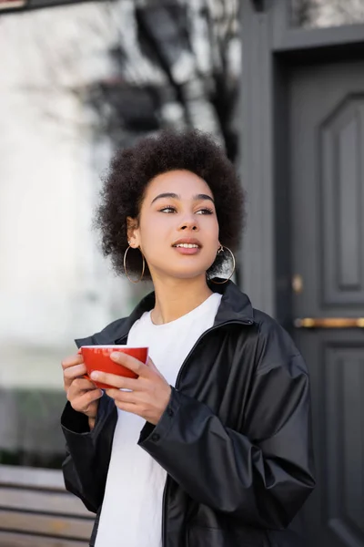 Mulher americana africana em casaco segurando xícara de café fora — Fotografia de Stock