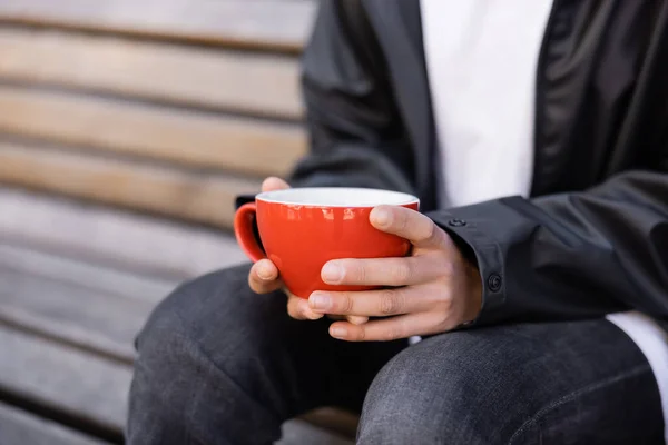 Cropped view of african american woman holding cup of coffee while sitting on bench — Foto stock