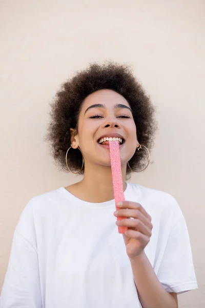 Happy african american young woman eating sweet jelly strip on white — Fotografia de Stock