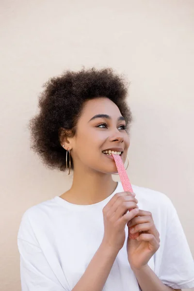 Задоволена афроамериканська молода жінка їсть солодку желе-бульбашкову стрічку на білому — стокове фото