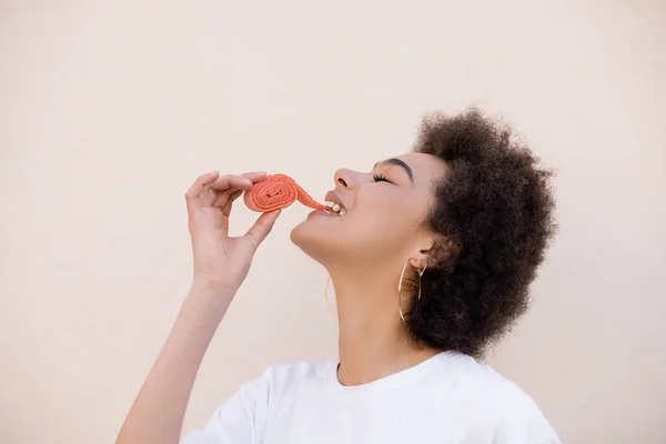 Feliz afro-americano jovem mulher comendo geléia bolha fita no branco — Fotografia de Stock