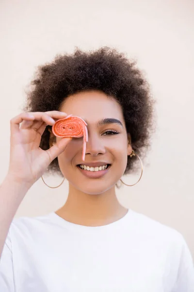 Happy african american young woman holding jelly bubble tape near eye on white — Stock Photo