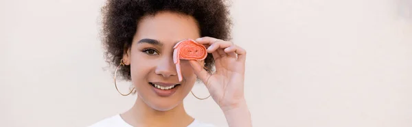 Feliz afro-americana jovem mulher cobrindo olho com fita de bolha de geleia no branco, banner — Fotografia de Stock