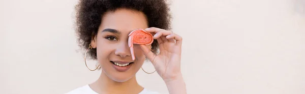 Glücklich afrikanisch-amerikanische junge Frau, die Auge mit Gummiblasenband auf weißem, Banner bedeckt — Stockfoto