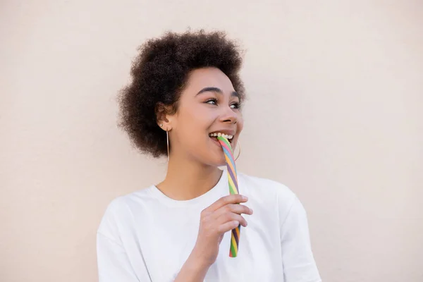 Mujer joven afroamericana positiva comiendo caramelos de jalea en blanco - foto de stock