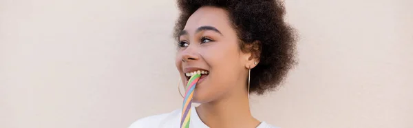 Позитивна афроамериканська молода жінка їсть желе цукерки на білому фоні, банер — стокове фото