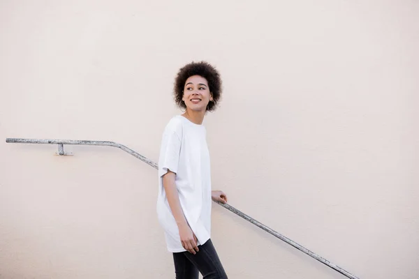 Smiling young african american woman walking near rusty handrail — стоковое фото