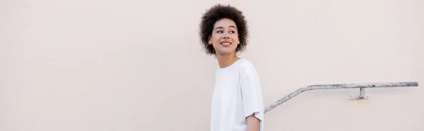 Smiling young african american woman walking near rusty handrail, banner — Stock Photo