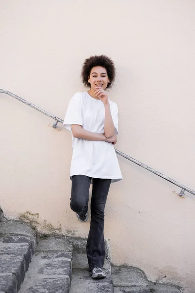 Full length of cheerful african american woman posing on stairs near rusty handrail — Stock Photo