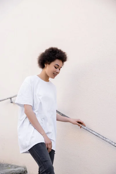 Cheerful african american woman walking near rusty handrail — Stockfoto
