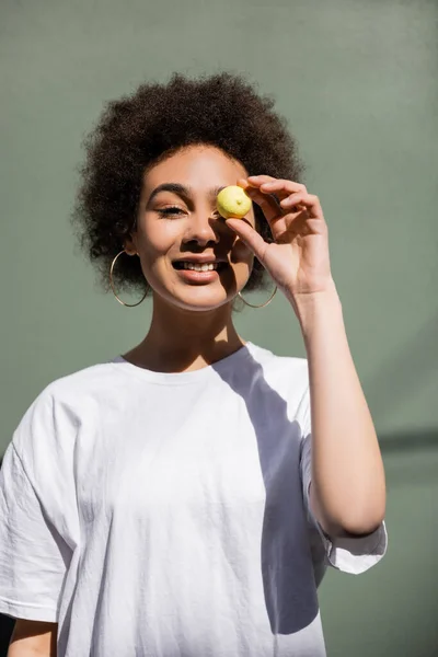 Cheerful african american woman covering eye with yellow candy — Foto stock