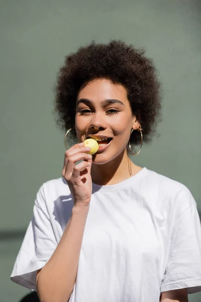 Alegre afroamericana mujer comiendo amarillo caramelo - foto de stock