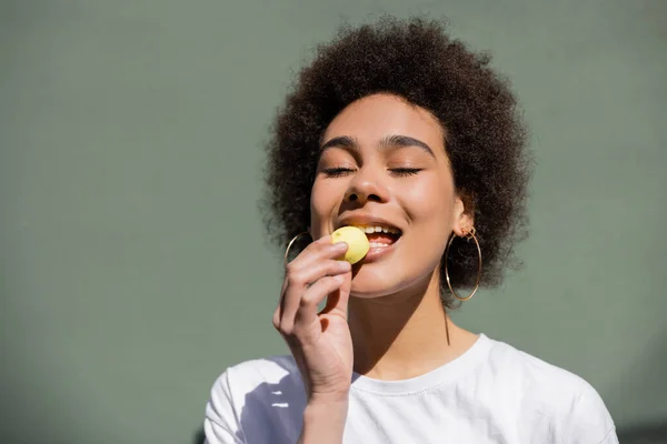 Pleased african american woman eating yellow candy — Fotografia de Stock