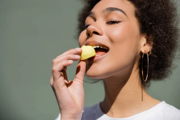 Pleased african american woman eating yellow candy - foto de stock