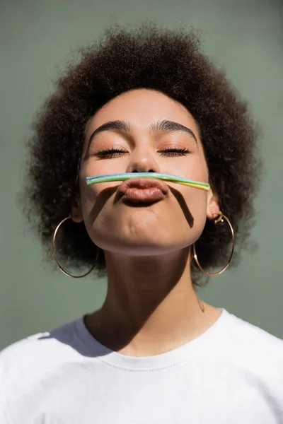 Curly african american woman holding jelly straw with mouth while grimacing outside — Stock Photo