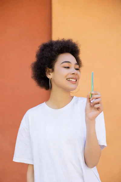 Joyful african american woman holding jelly straw near orange wall - foto de stock