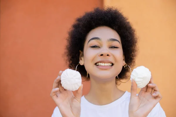 Happy african american woman holding zefir near orange wall — Stock Photo