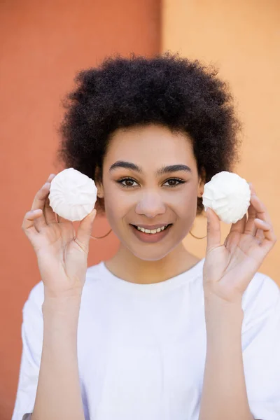 Smiling african american woman holding zefir near orange wall — Stock Photo
