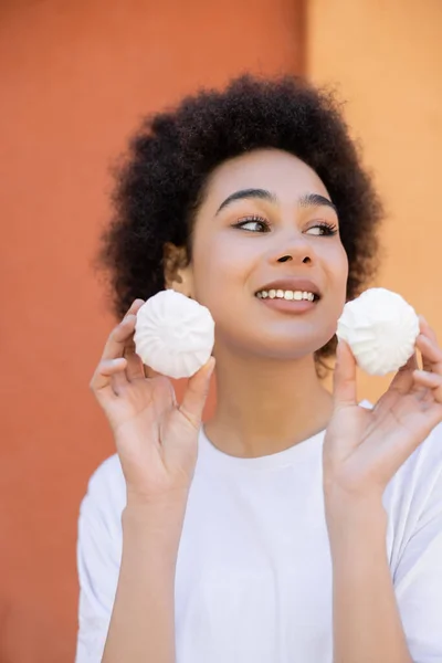 Pleased african american woman holding zefir near orange wall — Stock Photo