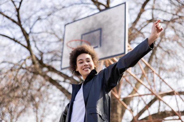 Vue à angle bas de femme afro-américaine heureuse debout avec la main tendue sur le terrain de basket-ball en plein air — Photo de stock
