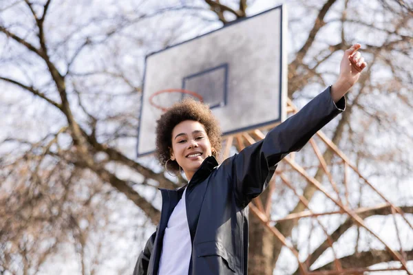 Low angle view of happy african american woman standing with outstretched hand on basketball outdoor court — стоковое фото