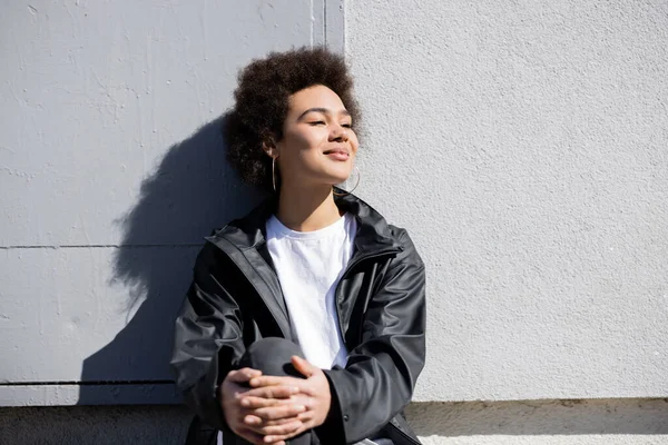 Happy african american woman in jacket leaning on wall — Stock Photo