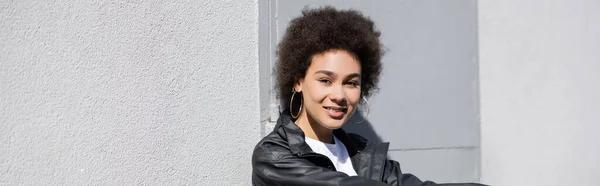 Mujer afroamericana feliz en chaqueta mirando a la cámara, pancarta - foto de stock