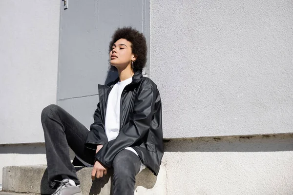 Sunshine on face of stylish african american woman sitting on stairs near wall — стоковое фото