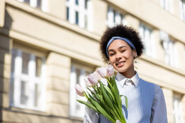 Sonriente afroamericana mujer sosteniendo tulipanes en la calle - foto de stock