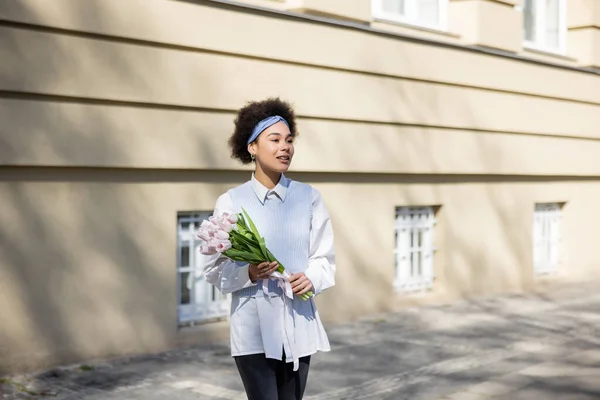 Pleased african american woman holding bouquet of tulips on street — Stockfoto