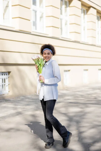 Young african american woman holding bouquet of tulips and smiling on street — Fotografia de Stock