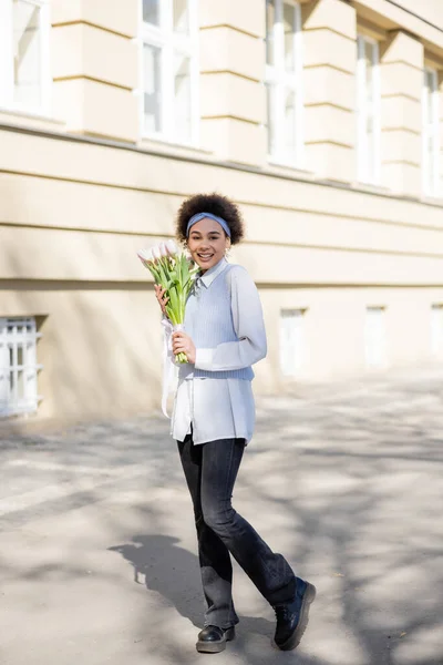 Young african american woman holding bouquet of tulips and smiling on street — Stock Photo