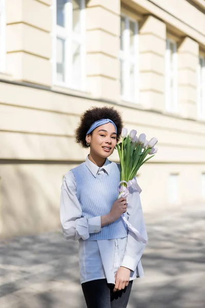 Junge afrikanisch-amerikanische Frau hält Tulpen und lächelt auf der Straße — Stockfoto