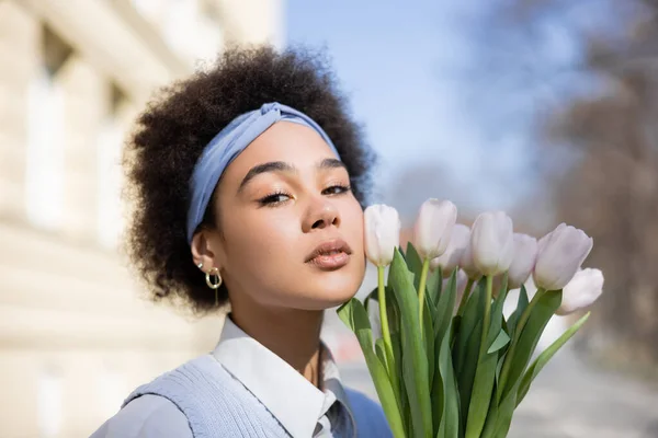 Young african american woman holding bouquet of tulips and looking at camera - foto de stock