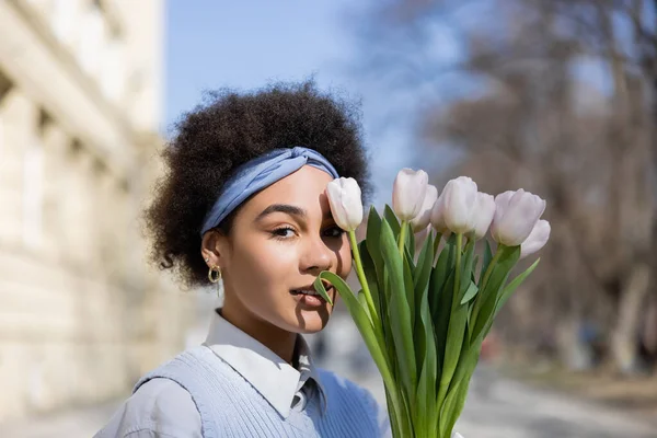 Junge afrikanisch-amerikanische Frau blickt in die Kamera in der Nähe von Tulpenstrauß — Stockfoto