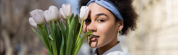 Jeune femme afro-américaine regardant la caméra près du bouquet de tulipes, bannière — Photo de stock