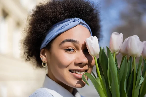 Positivo joven afroamericana mujer mirando cámara cerca ramo de tulipanes - foto de stock