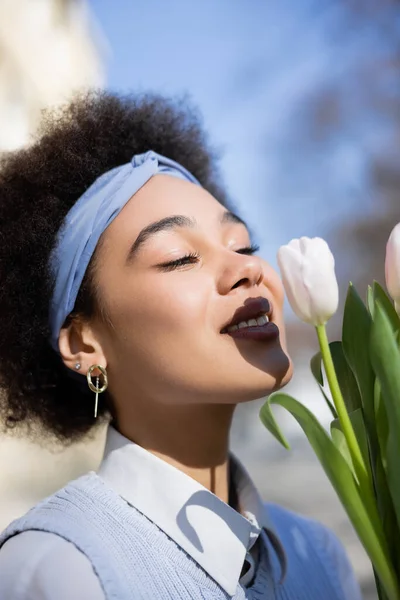 Positiva joven afroamericana mujer buscando ramo de tulipanes - foto de stock