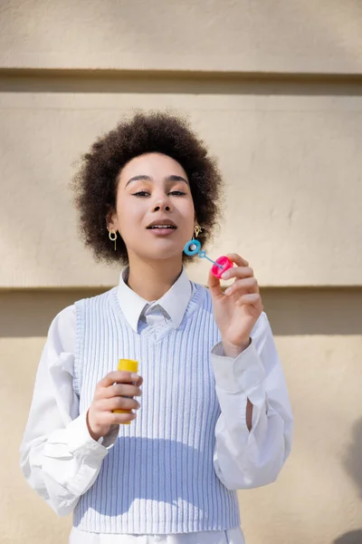 Curly african american woman in blue vest and white shirt holding bubble wand — Stock Photo