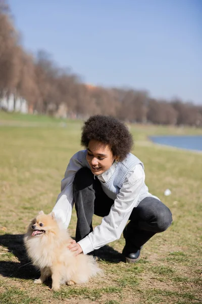 Smiling african american woman cuddling pomeranian dog - foto de stock