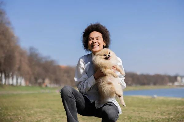 Happy african american woman holding in arms pomeranian dog — Stock Photo